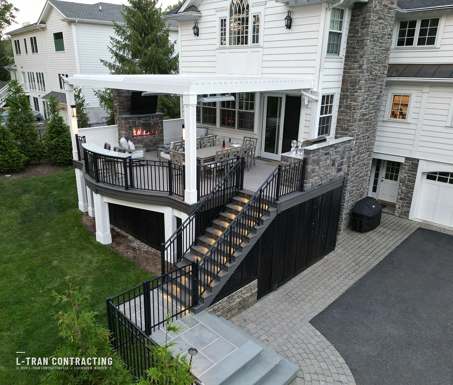 Multi-level deck with outdoor stone fireplace and pergola at dusk