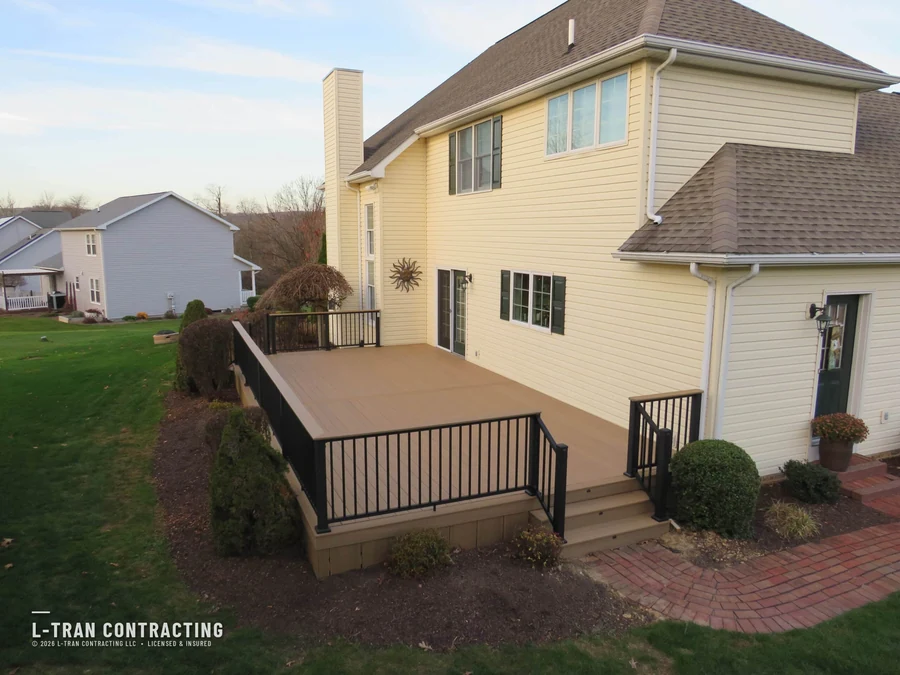 Elevated composite deck with black railings over brick patio