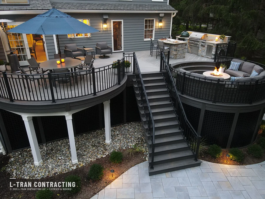Two-level curved deck with built-in fire pit lounge and outdoor kitchen at dusk